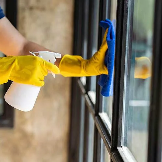 Nahaufnahme der Hand eines Restaurantmitarbeiters, die während des Ausbruchs des Virus ein Fensterglas reinigt und Desinfektionsmittel versprüht. Verwenden Sie einen Reiniger oder verwenden Sie Alkohol, um das Restaurant zu desinfizieren