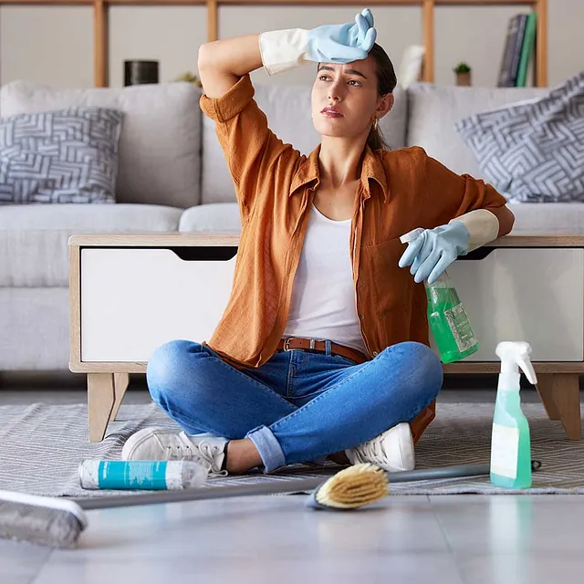 Müde Frau putzt und sitzt auf dem Wohnzimmerboden mit Reinigungsmittel, Chemikalien oder Desinfektionsspray für die Hygiene zu Hause. Hausangestellte erschöpft von Hauswirtschaft, Hausarbeit oder sauberer Wohnung