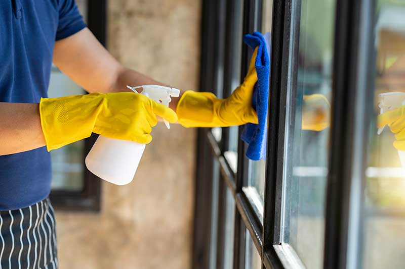 Nahaufnahme der Hand eines Restaurantmitarbeiters, die während des Ausbruchs des Virus ein Fensterglas reinigt und Desinfektionsmittel versprüht. Verwenden Sie einen Reiniger oder verwenden Sie Alkohol, um das Restaurant zu desinfizieren